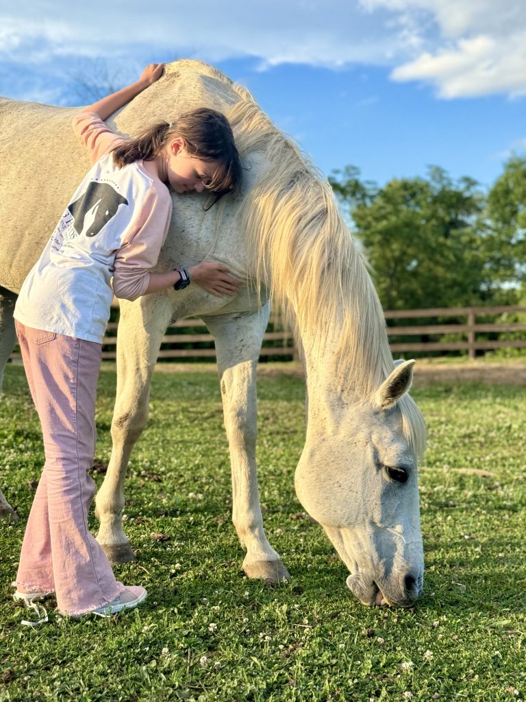 Girl leaning against a white horse with eyes closed.
