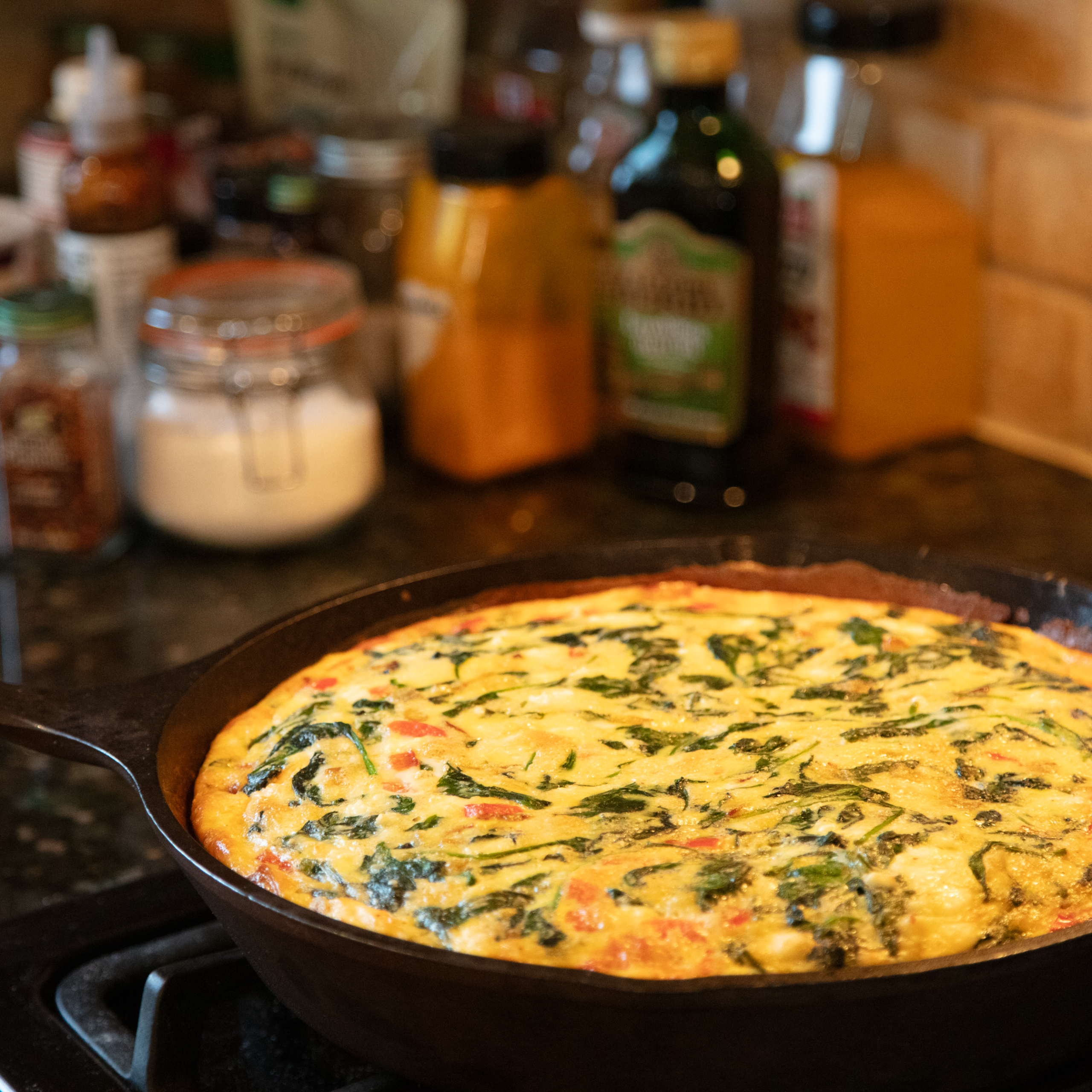 cast iron pan with vegetable frittata on stove with spices in the background