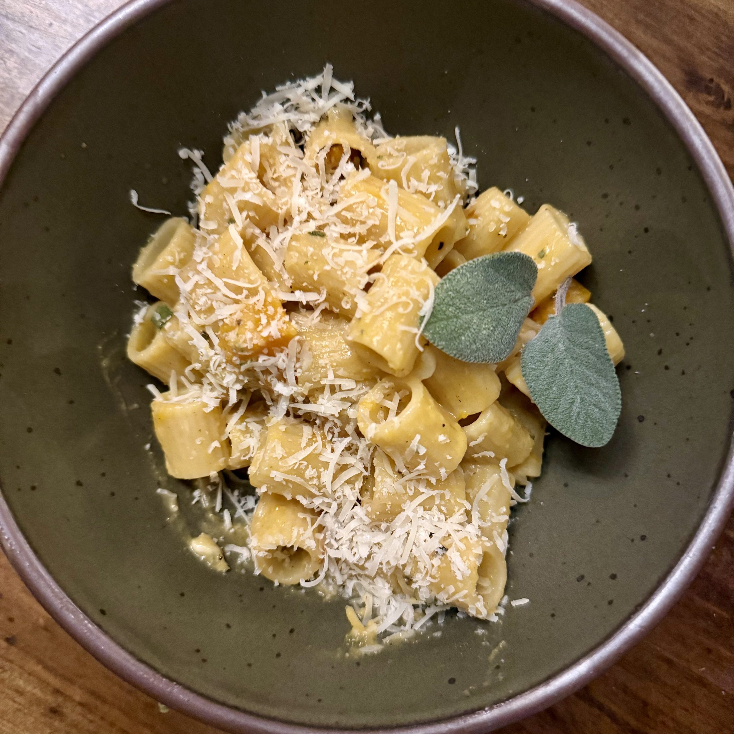 green bowl with pasta, fresh sage, and parmesan cheese